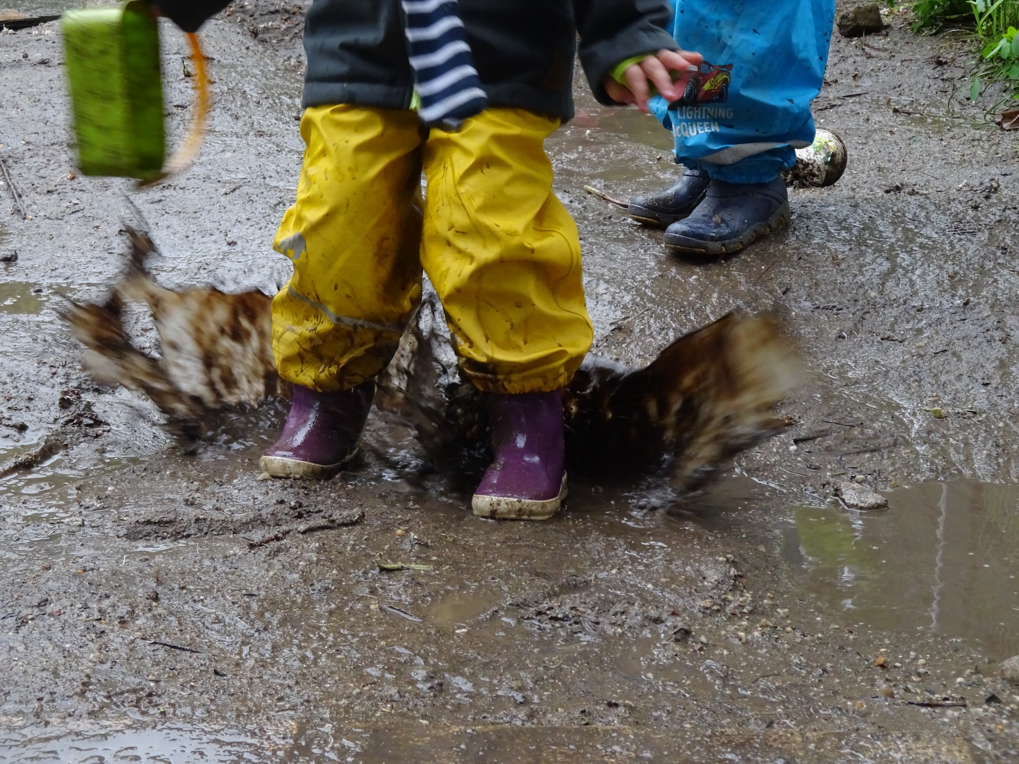 Kinderfüße in Gummistiefeln im Schlamm